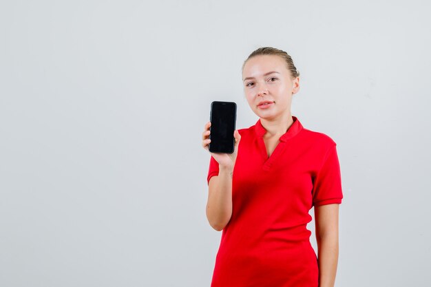 Señorita sosteniendo teléfono móvil en camiseta roja y mirando alegre