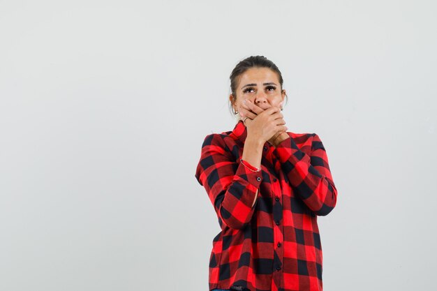 Señorita tomados de la mano en la boca en camisa a cuadros y mirando pensativo