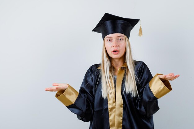 Señorita en traje académico extendiendo las palmas a un lado y mirando confiado