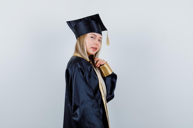 Señorita en traje académico posando mientras está de pie y luciendo hermosa