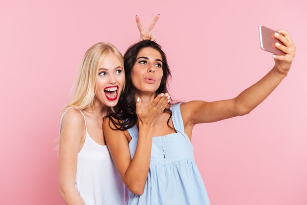 Señoritas divertidas haciendo selfie y sonriendo aislado