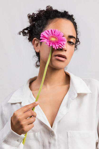 Sensual mujer con flor cubriendo ojo.