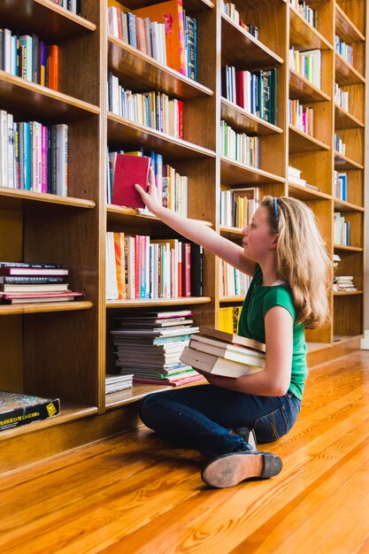 Sentado en la chica del piso poniendo el libro en el estante