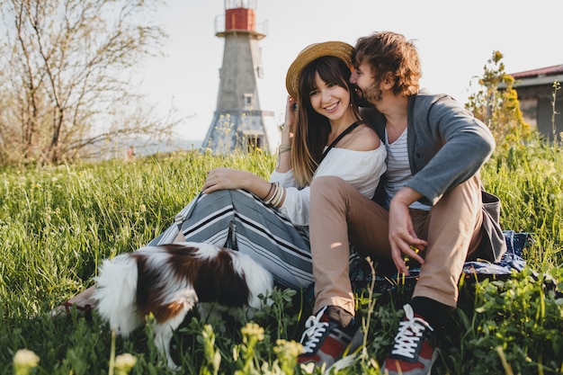 Sentado en la hierba joven pareja hipster elegante enamorado caminando con perro en campo