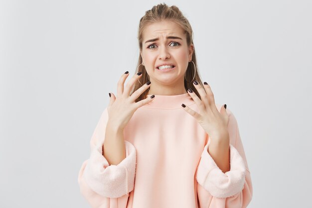 Sentimiento y emociones humanas. Insatisfecha hermosa chica caucásica con cabello rubio vestido con una sudadera rosa que muestra su disgusto y aversión a algo que no le gusta, frunciendo el ceño.