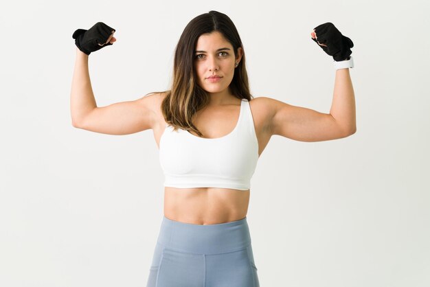 Sentirse poderoso después de levantar pesas. Hermosa mujer fuerte de unos 20 años mostrando sus bíceps. Mujer caucásica atlética trabajando