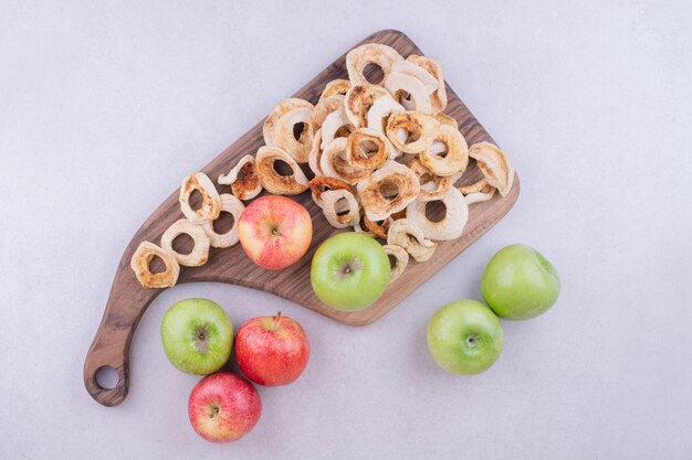 Seque las rodajas de manzana con manzanas frescas sobre tabla de madera en gris.
