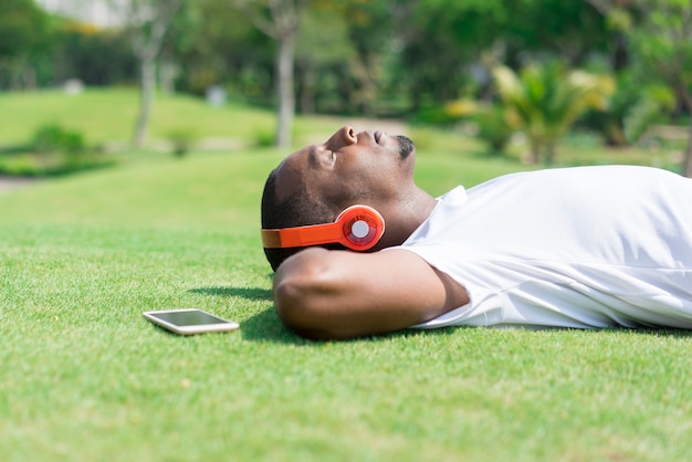 Sereno hombre negro descansando en el parque y escuchando música.