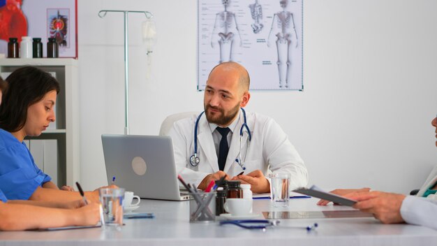 Sergeon presenta a sus colegas nuevos procedimientos médicos, compañeros de trabajo que toman notas con una lluvia de ideas sentados en el mostrador de reuniones en la clínica del hospital. Equipo profesional hablando durante la conferencia de salud