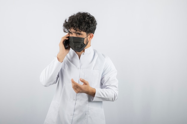 Seria conversación por teléfono. Doctor joven de pelo rizado que habla con el teléfono.