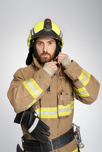 Foto gratuita serio bombero masculino en uniforme con casco de protección retrato interior de un tipo fuerte en