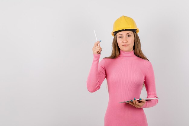 En serio, la chica ingeniera está mirando a la cámara levantando un bolígrafo sobre fondo blanco.