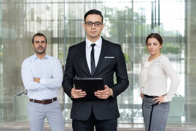 Serio empresario confía en pie frente a sus colegas