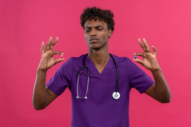 Un serio joven apuesto médico de piel oscura con cabello rizado vistiendo uniforme violeta con estetoscopio mirando pastillas