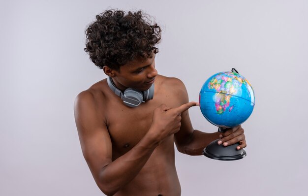 Un serio joven guapo de piel oscura con cabello rizado usando audífonos apuntando al globo con el dedo índice