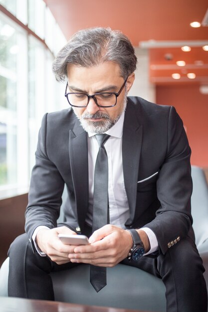 Serio líder de negocios utilizando el teléfono inteligente en el vestíbulo