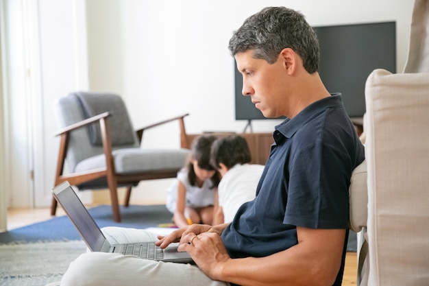 Serio profesional trabajando en casa, sentado en el suelo y usando la computadora portátil