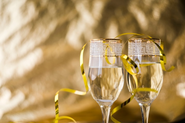 Serpentinas doradas sobre copas de champán transparentes contra un fondo borroso