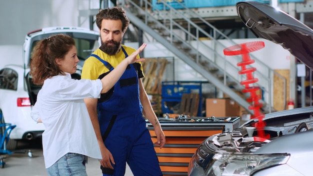 Serviceman en el servicio de automóviles usando realidad aumentada holográfica para mostrar al cliente el pistón defectuoso del vehículo Empleado de garaje trabajador usando innovadora tecnología AR para proyectar piezas de automóviles para mujer