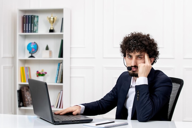 Servicio al cliente apuesto hombre rizado en traje de oficina con computadora y auriculares cansado y molesto