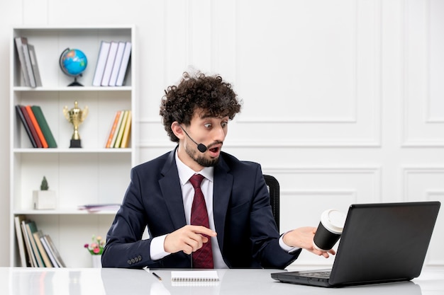 Servicio al cliente apuesto joven en traje de oficina con computadora portátil y auriculares derramando café