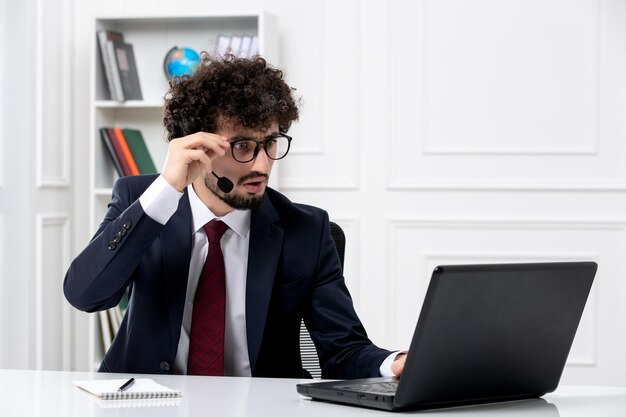 Servicio al cliente apuesto joven en traje de oficina con computadora portátil y auriculares con gafas puestas