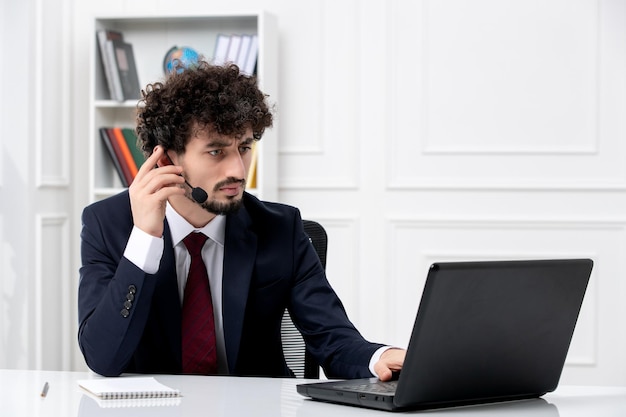 Servicio al cliente apuesto joven en traje de oficina con computadora portátil y auriculares en la llamada seria