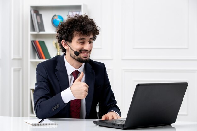 Servicio al cliente apuesto joven en traje de oficina con computadora portátil y auriculares sonriendo felizmente