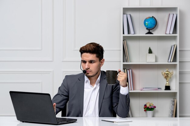 Servicio al cliente bastante caballero con computadora en traje de oficina gris con auriculares y café