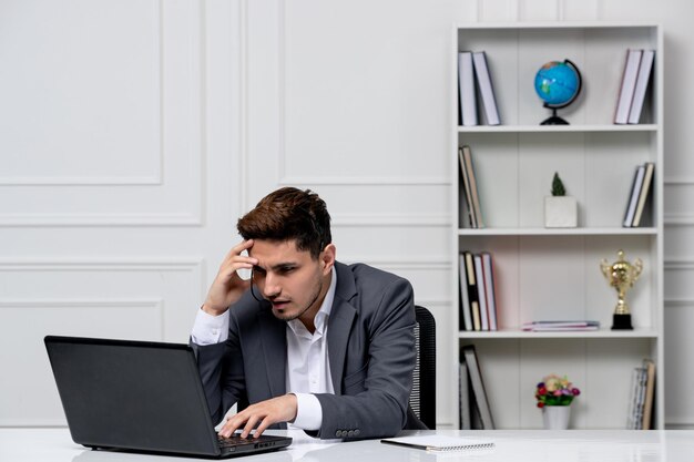 Servicio al cliente bastante caballero con computadora en traje de oficina gris confundido durante el trabajo