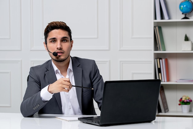 Servicio al cliente bastante caballero con computadora en traje de oficina gris con lápiz