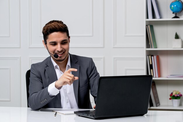 Servicio al cliente bastante caballero con computadora en traje de oficina gris sonriendo en la videollamada