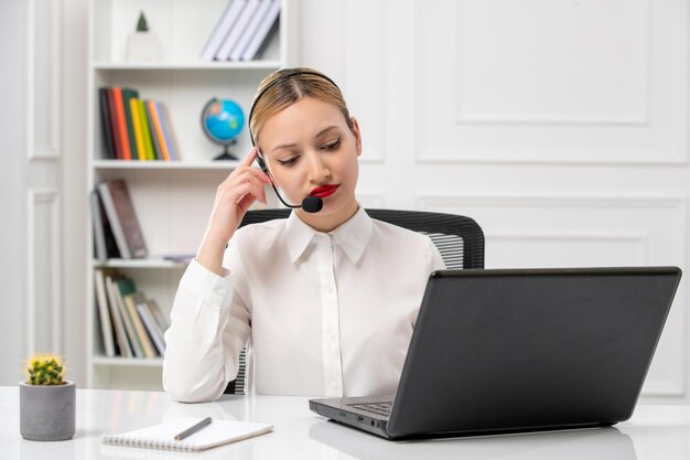 Servicio al cliente linda chica rubia con camisa blanca y computadora portátil y auriculares cansados con las manos en la cabeza