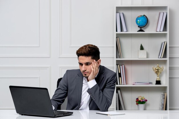 Servicio al cliente lindo chico guapo en traje de oficina con computadora mirando en una pantalla y enfocado
