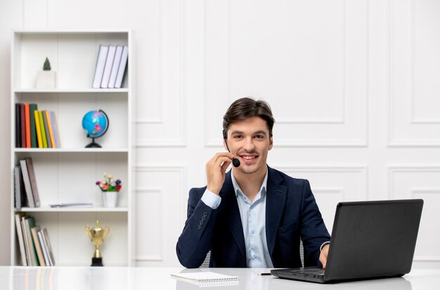 Servicio al cliente el lindo chico moreno en el traje con computadora portátil con micrófono y auriculares