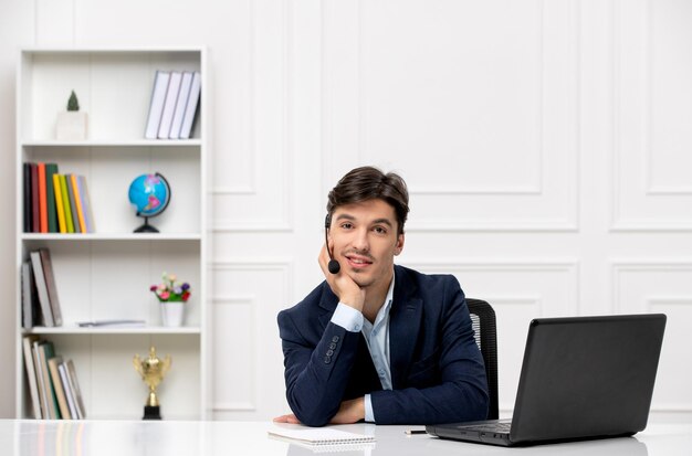 Servicio al cliente, el lindo chico moreno en el traje con una computadora portátil sonriendo con auriculares