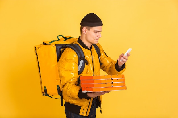 Servicio de entrega sin contacto durante la cuarentena. El hombre entrega comida y bolsas de compras durante el aislamiento. Emociones del repartidor aislado en amarillo