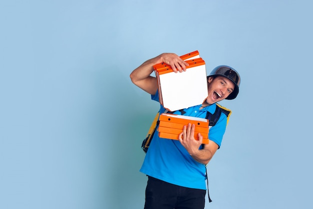 Servicio de entrega sin contacto durante la cuarentena. El hombre entrega comida y bolsas de compras durante el aislamiento. Emociones del repartidor aislado en azul