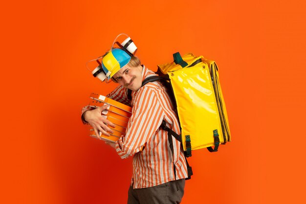 Servicio de entrega sin contacto durante la cuarentena. El hombre entrega comida y bolsas de compras durante el aislamiento. Emociones del repartidor aislado en naranja