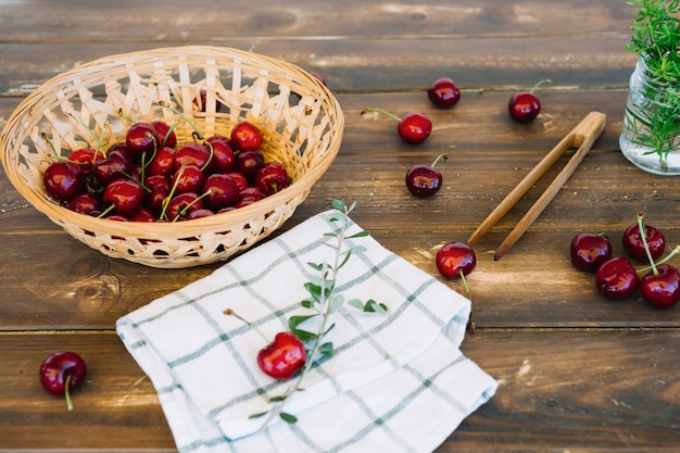 Servilleta y cerezas rojas en cuenco de mimbre en superficie de madera