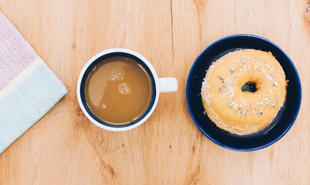 Servilleta; taza de café; buñuelo sobre fondo de madera