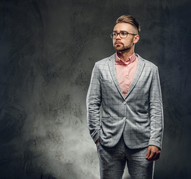 Sesión de estudio de un hombre elegante y atractivo con traje a cuadros, gafas y camisa rosa. Puso una mano en su bolsillo.