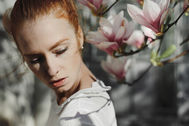 Sesión de fotos de mujer pelirroja cerca de flores de magnolia