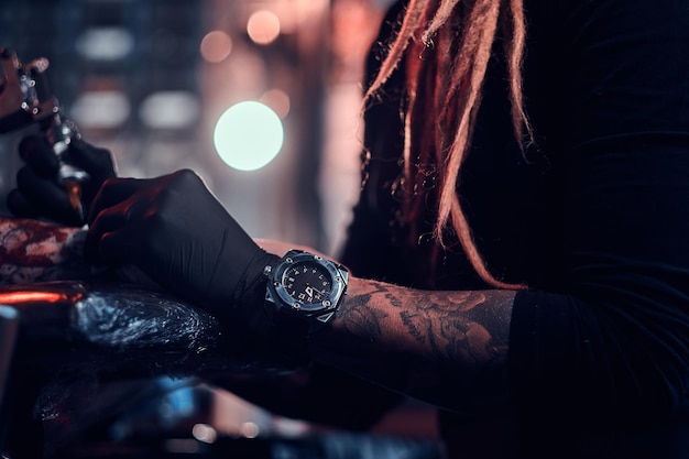 Sesión de fotos de primer plano de la fabricación de tatuajes, el artista está trabajando con una máquina de tatuajes en la mano del cliente.