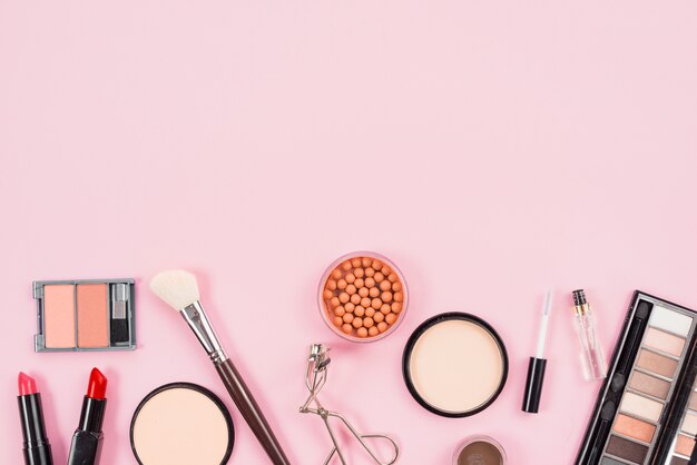 Set de maquillaje y productos de belleza estética sobre fondo rosa.