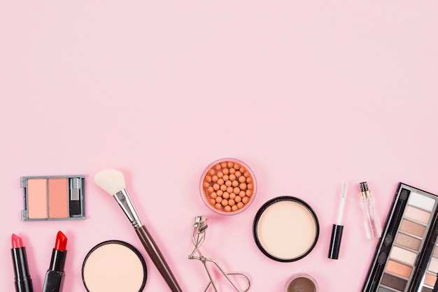 Set de maquillaje y productos de belleza estética sobre fondo rosa.