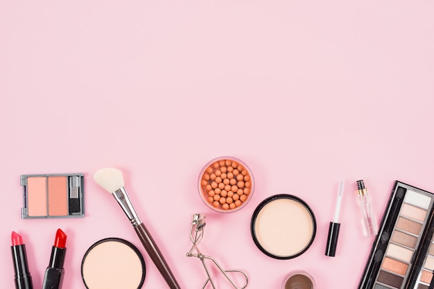 Set de maquillaje y productos de belleza estética sobre fondo rosa.