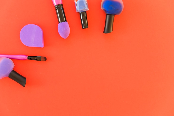 Foto gratuito set de pinceles de maquillaje profesional imprescindible; esmalte de uñas y esponja sobre fondo rojo