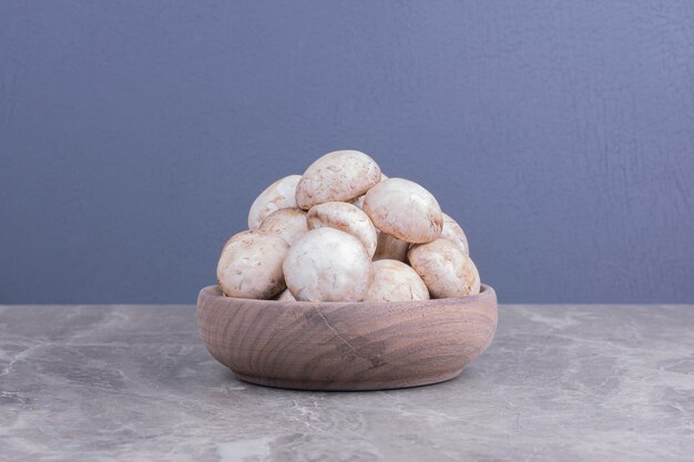 Setas blancas en una taza de madera sobre superficie gris