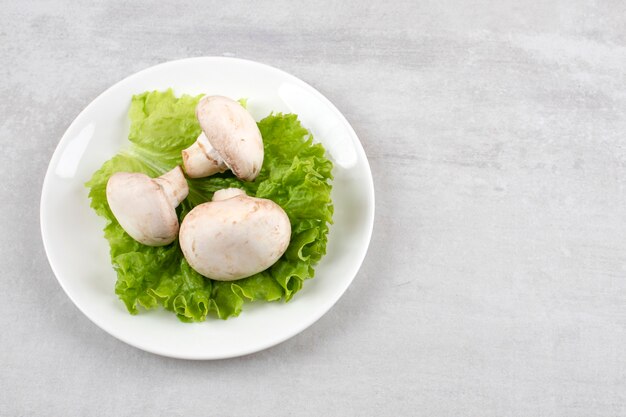 Setas en una hoja de lechuga en un plato, sobre la mesa de mármol.